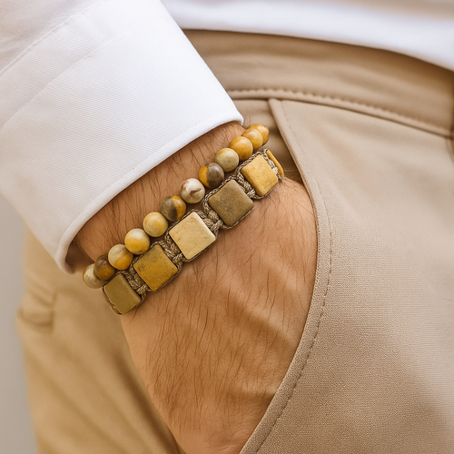 Cosmic Collections Jupiter set herenarmbanden – handgemaakte verstelbare vierkante natuursteen armband en elastische kralenarmband in beige en goudtinten gedragen bij wit overhemd en zandkleurige pantalon